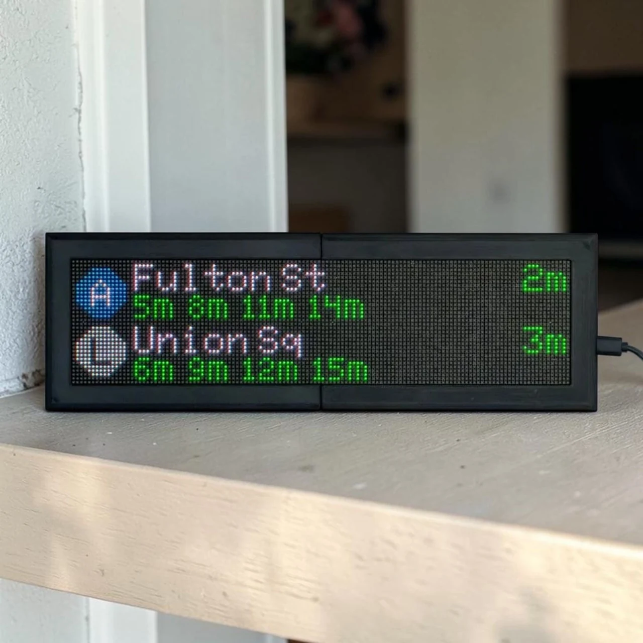 CommuteLive display on a walnut desk showing NYC subway arrivals